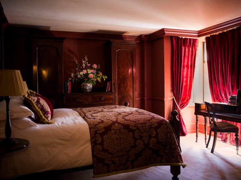 Spacious Luxury Double bedroom at Batty Langley's, Spitalfields – red furnishings, antique desk, and floral display.