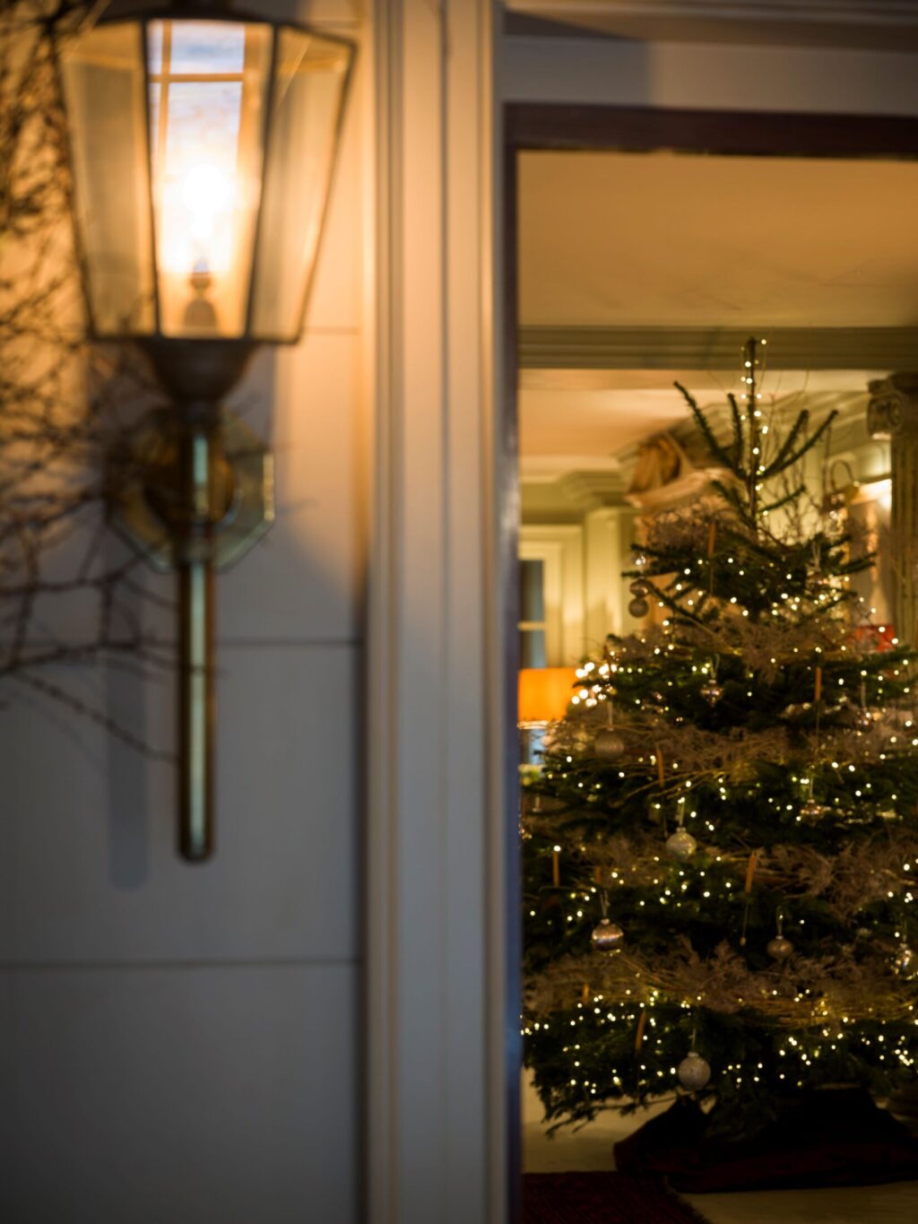 A warmly lit exterior lantern beside an open doorway at Batty Langley’s, revealing a glowing Christmas tree inside.