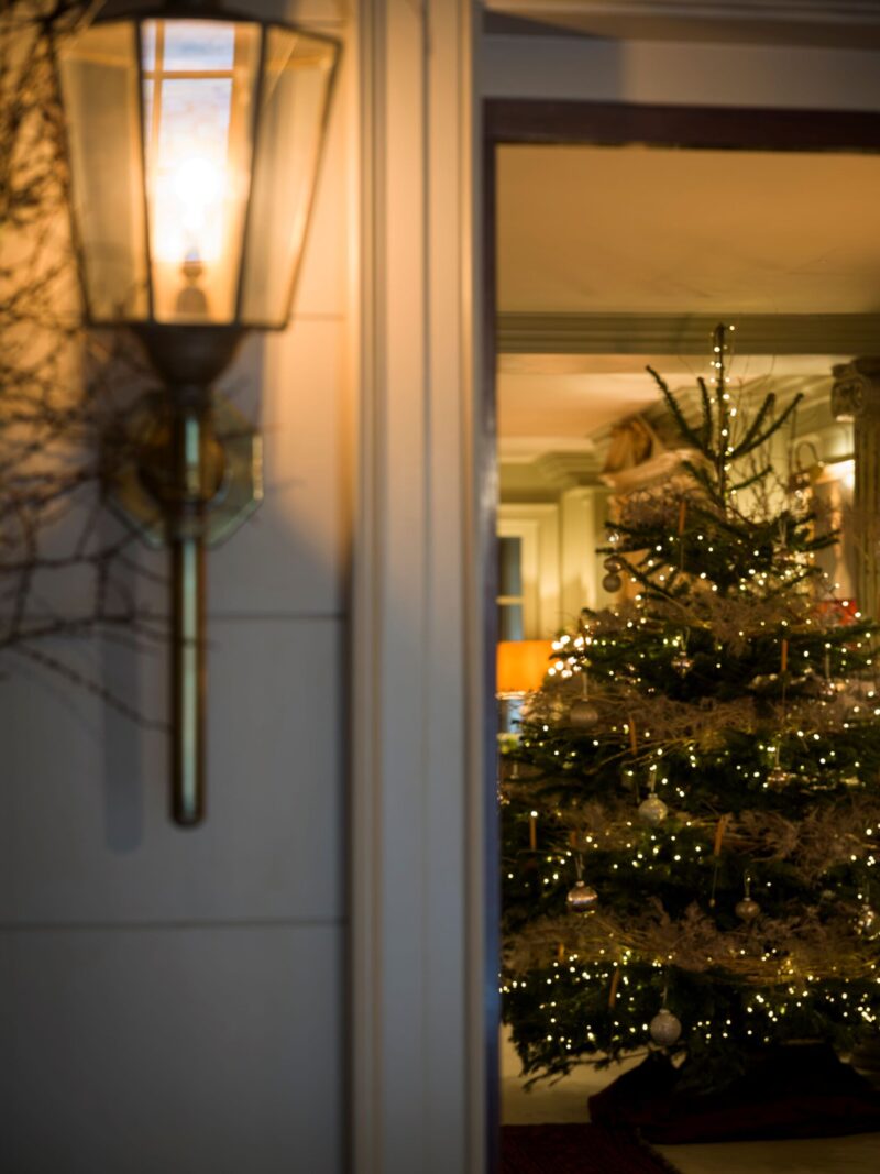 A warmly lit exterior lantern beside an open doorway at Batty Langley’s, revealing a glowing Christmas tree inside.