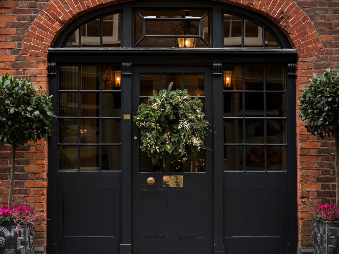 Festive wreath on the black Georgian front door of Batty Langley’s, framed by red brick and topiary plants.
